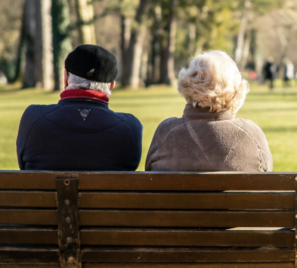 an elderly man and woman sitting no a park bench together, seen from behind
